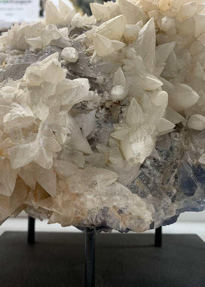 Large natural calcite on fluorite mineral specimen with pale crystal growth mounted on a black display stand at Earthforged Rock Shop.