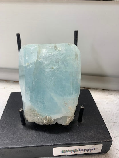 Large natural pale blue aquamarine crystal specimen displayed on black stand at Earthforged