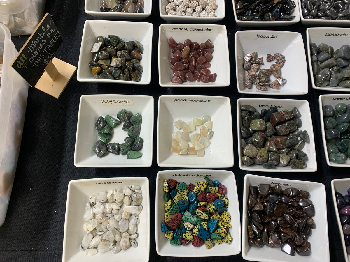 Small natural gemstones and mineral specimens displayed in individual trays at Earthforged.