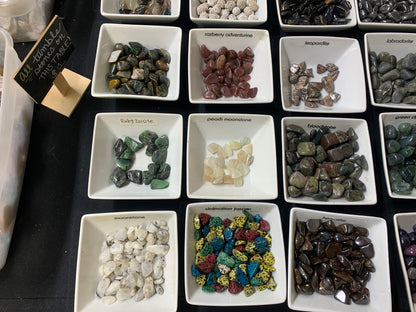 Small natural gemstones and mineral specimens displayed in individual trays at Earthforged.